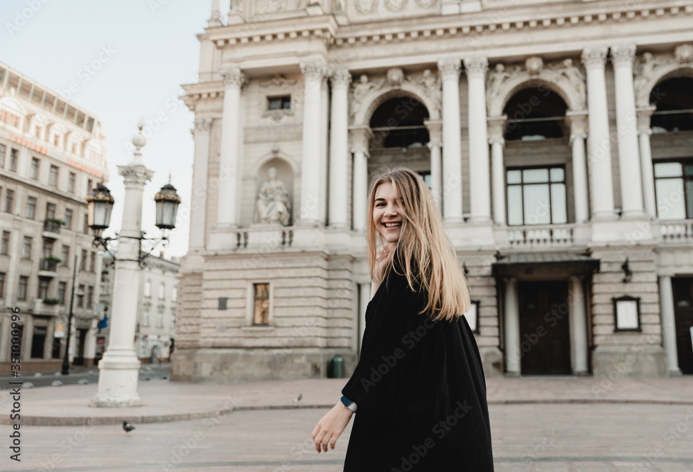 A beautiful young woman in a black dress with blond hair walks around the city with a bag with red flowers, filtered image, flare sunshine A beautiful young woman in a black dress with blond hair walks around the city with a bag with red flowers, filtered image, flare sunshine