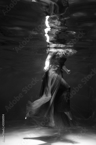 Fototapeta Naklejka Na Ścianę i Meble -  Black and white photo. Beautiful girl underwater in a red dress swims in the pool. Tenderness and elegance. Bubbles and a lot of water