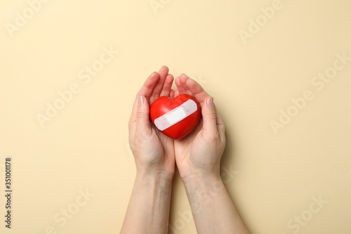 Female hands hold heart with adhesive plaster on beige background, top view