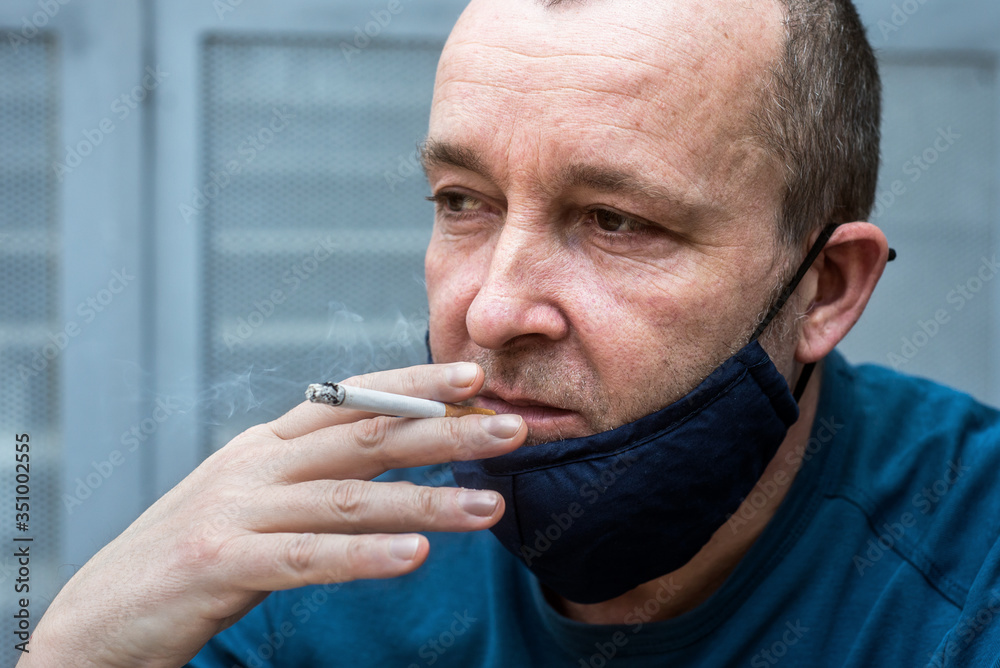 Portrait of caucasian man smoking a cigarette with a homemade fabric mask in the street during the covid-19 pandemic Portrait of caucasian man smoking a cigarette with a homemade fabric mask in the street during the covid-19 pandemic