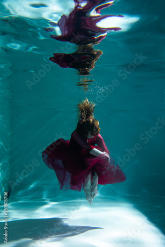 Beautiful girl underwater in a red dress swims in the pool. Tenderness and elegance. Bubbles and a lot of water