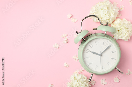 Alarm clock and beautiful hydrangea flowers on pink background