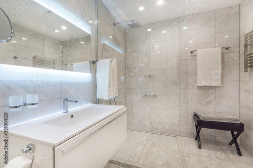 Beautiful modern bathroom with large backlit illuminated mirror  sink  and glass shower