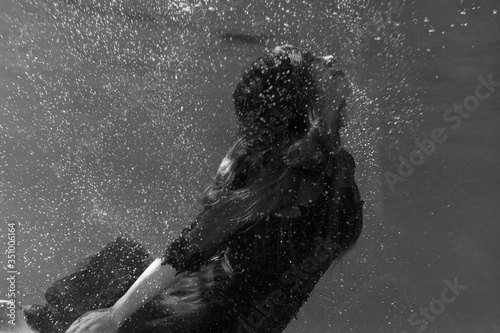 Black and white photo. Beautiful girl underwater in a red dress swims in the pool. Tenderness and elegance. Bubbles and a lot of water
