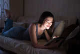 Smiling girl looking at the tablet in the dark at night