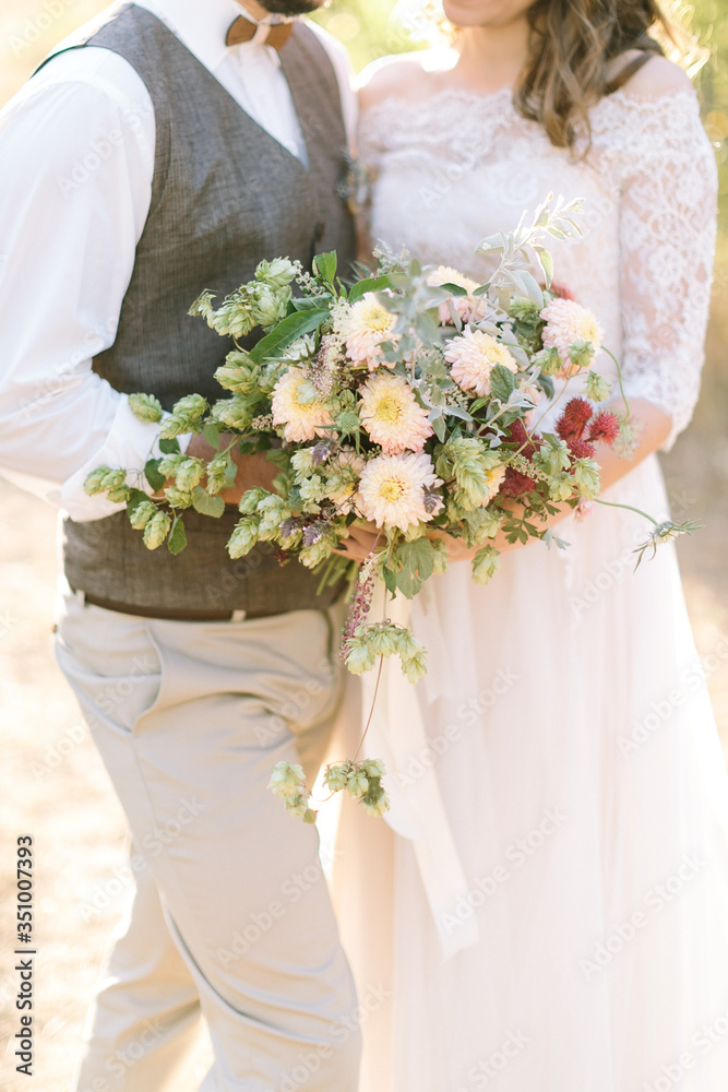 filled with light, a gentle cropped frame where the bride and groom hug each other holds a sloppy bouquet flowers.