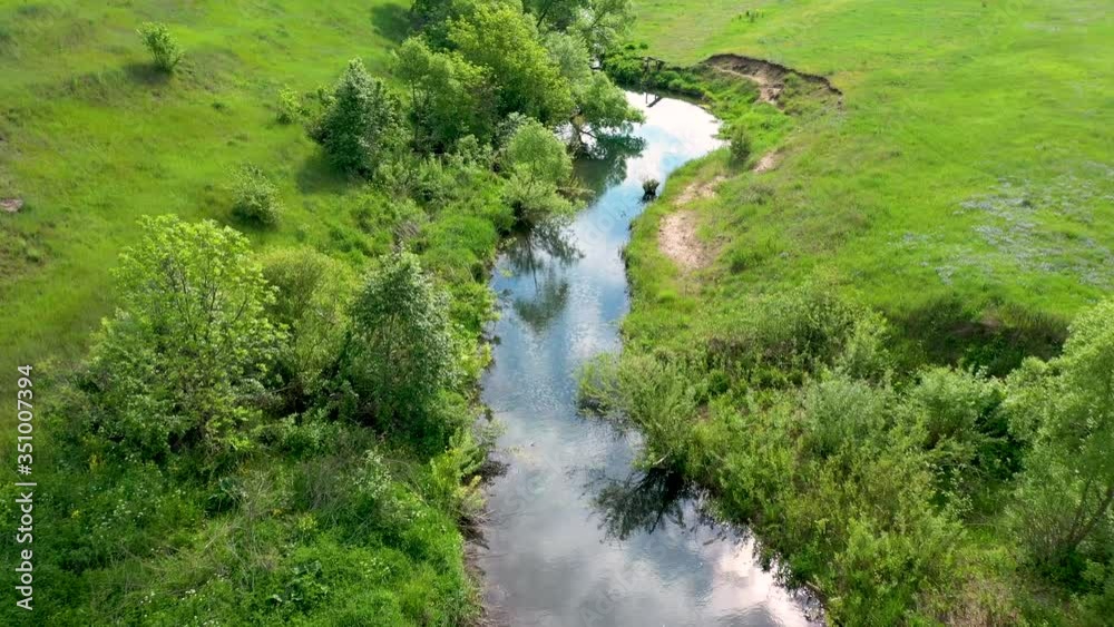 Aerial video, flying a quadcopter over a small winding river that reflects the blue sky with white clouds and the sun Aerial video, flying a quadcopter over a small winding river that reflects the blue sky with white clouds and the sun