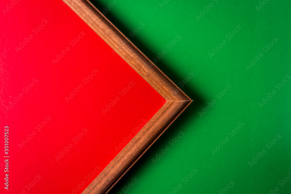 Fototapeta premium Wooden frame on a green background. Inside the frame is a red background. The frame occupies half the space. empty space for an inscription.