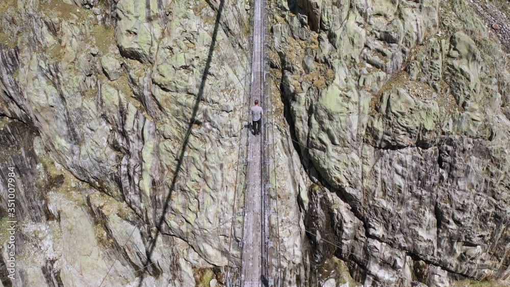 Aerial shot of man walking on extreme pendant bridge between giant mountains Aerial shot of man walking on extreme pendant bridge between giant mountains