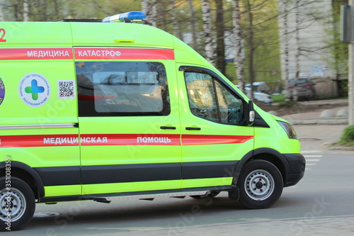 White ambulance with a red stripe with blue flashing lights on a city street in Russia.