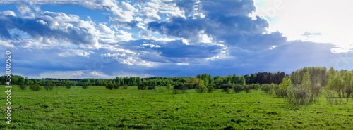 Landscape spring cloudy sky before sunset field and forest in the background