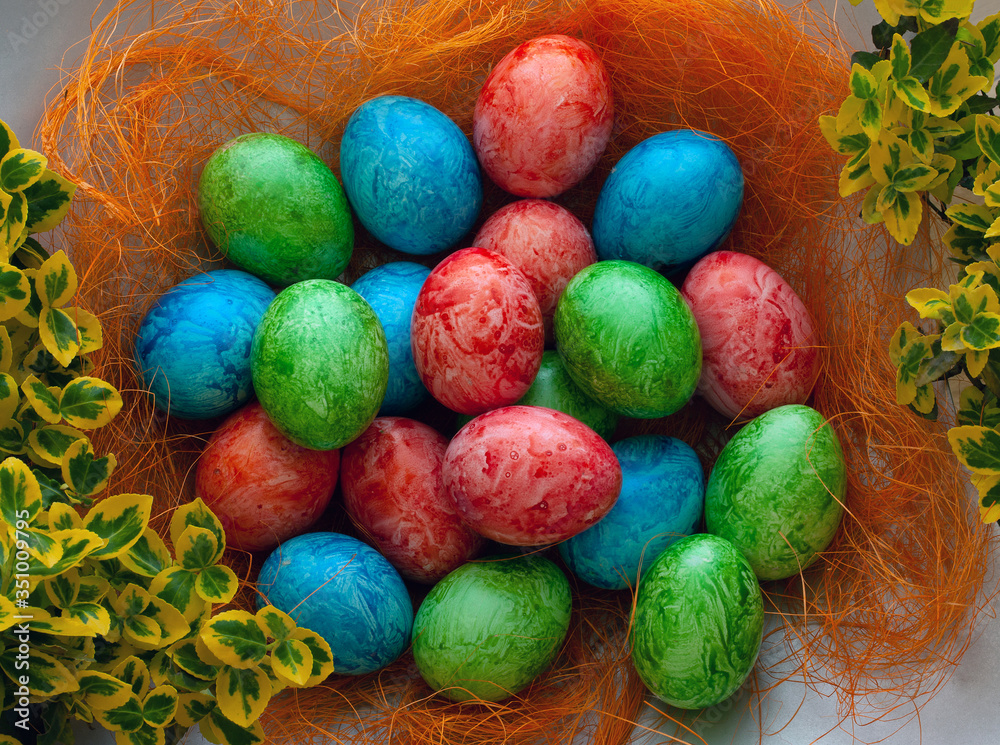 Colorful Easter holiday eggs, arranged with green twigs and an orange wreath of grass on a white background. Colorful Easter holiday eggs, arranged with green twigs and an orange wreath of grass on a white background.
