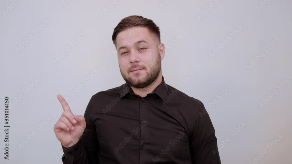 Young Bearded Dark Haired Man In Black Stylish Shirt On White Background, Focused Male Lifted Forefinger Up And Thinks. The Concept Of Smart People, Intellectuals Young Bearded Dark Haired Man In Black Stylish Shirt On White Background, Focused Male Lifted Forefinger Up And Thinks. The Concept Of Smart People, Intellectuals