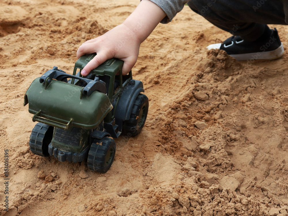 toy tractor and hand of a boy child. the kid plays in the sandbox with a toy. concept of child development, leisure or choice of future profession. toy tractor and hand of a boy child. the kid plays in the sandbox with a toy. concept of child development, leisure or choice of future profession.