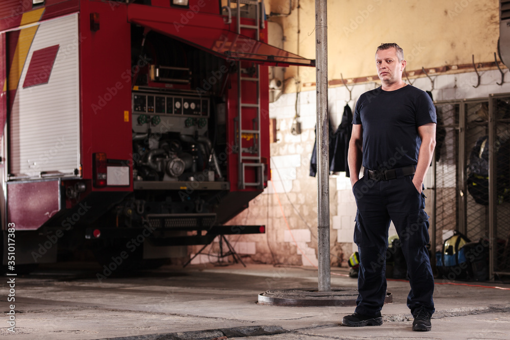 Professional fireman portrait. Firefighter wearing uniform of shirt and trousers. Fire truck in the background.