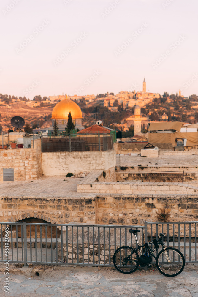 Fototapeta premium View of Old Jerusalem from the Mount. View of old city from the roof, with lattice and bicycle on foreground. Sunset time over Jerusalem. Jerusalem day. Holy places. Streets of jerusalem