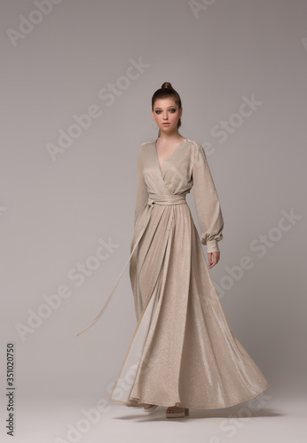 Photo A woman in a long evening golden dress steps and poses in a full-length studio