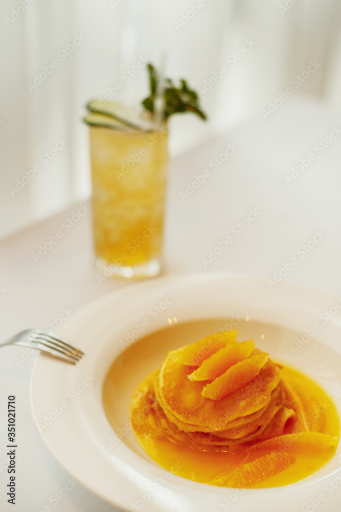 Pancakes with orange on a white plate and lemonade Pancakes with orange on a white plate and lemonade