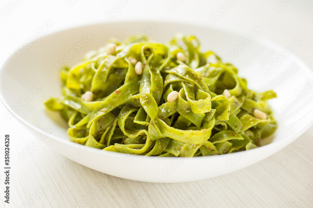 Close up Spinach Tagliatelle pasta with pine nuts and pesto sauce on white plate, selective focus.
