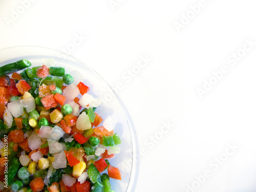 frozen vegetables (string beans, peas, corn, carrots, peppers) on a transparent plate on a white background. The view from the top.