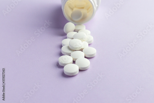 White capsules from a bottle on a lilac background. Epidemic, painkillers, health care, medicinal pills, and the concept of drug abuse