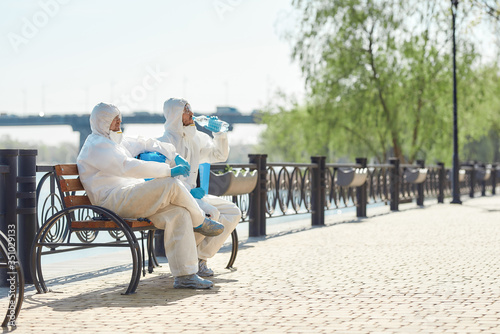 Time to rest. Sanitization, cleaning and disinfection of the city due to the emergence of the Covid19 virus. Specialized team in protective suits and masks takes a break near the riverside