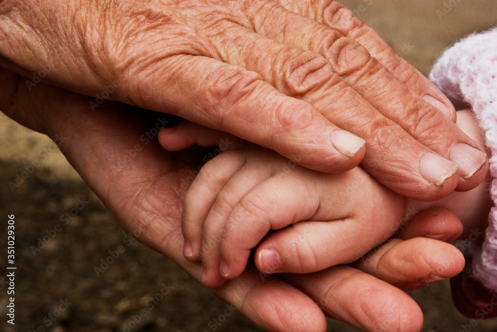 Grandmother's old wrinkled hands gently touches the small arms of a child close-up. Little toddler is playing with an old grandmother. Hands of a child and old grandmother close-up Grandmother's old wrinkled hands gently touches the small arms of a child close-up. Little toddler is playing with an old grandmother. Hands of a child and old grandmother close-up