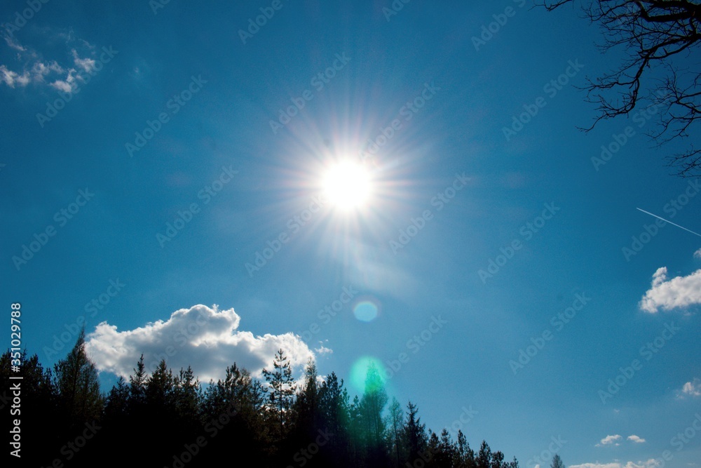 Sun burst. The afternoon sun is burning. Blue sky and a few white clouds.Sun and sunbeams in the azure sky and diffraction glow. Sun burst. The afternoon sun is burning. Blue sky and a few white clouds.Sun and sunbeams in the azure sky and diffraction glow.