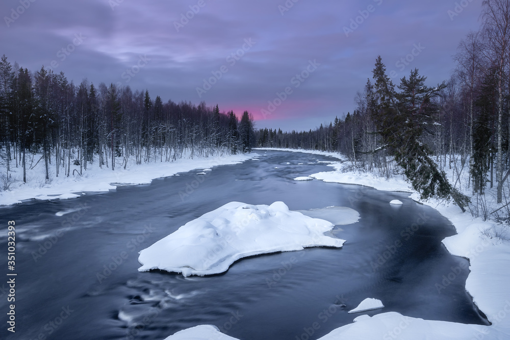 A winter landscape with river and floating ice island north of the Arctic Circle in Finnish Lapland