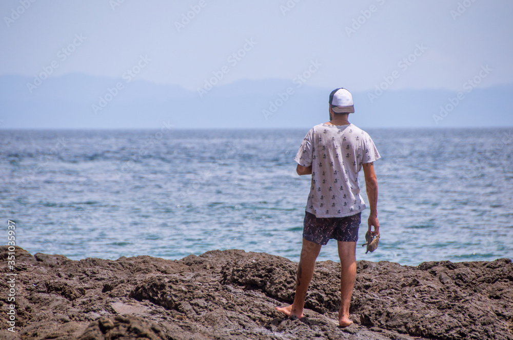 A man standing at the rocks looking at the horizon at the sea.