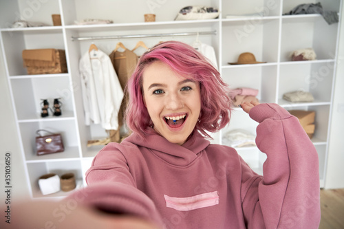 Excited hipster gen z teen girl fashion social media channel blogger stylist with pink hair piercing wear hoodie look at camera record vlog video tutorial in front of clothes wardrobe, face headshot. photo