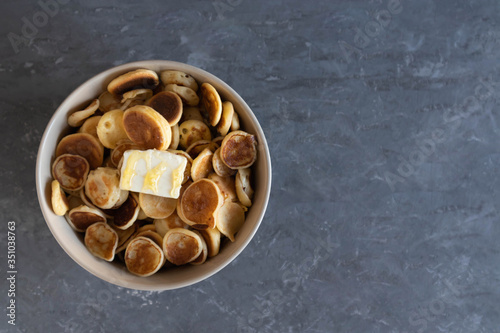 Tiny pancakes, small pancakes with butter and honey, on a concrete background in a bowl, flat lay.