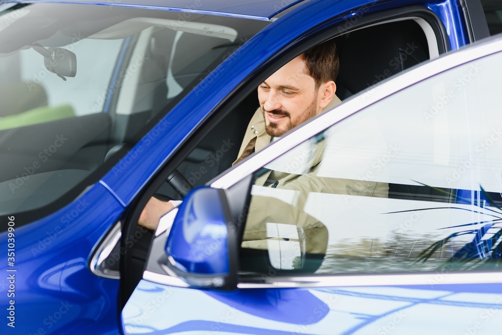 Handsome bearded businessman is sitting in a new car in car dealership Handsome bearded businessman is sitting in a new car in car dealership