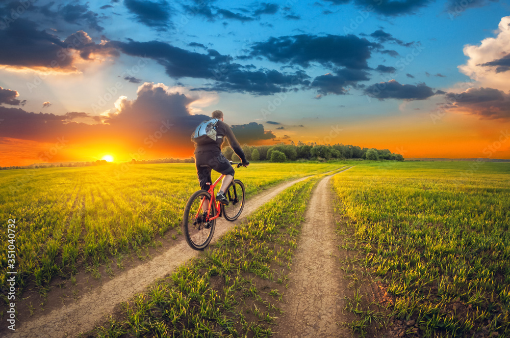 Fototapeta premium Ride of bike on a dirt road in a field at sunset.
