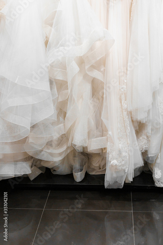 Cloth of wedding dresses made of silk chiffon, tulle, lace. Vertical photo for social networks. Beautiful White cream bridal dress on hangers in wedding salon. Pearls, crystals pendants on the sleeves