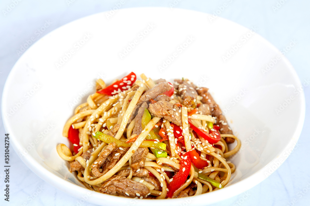 Udon with chicken and mushrooms-wheat noodles, chicken fillet , zucchini, paprika, sesame, mushrooms. Plate on a white background