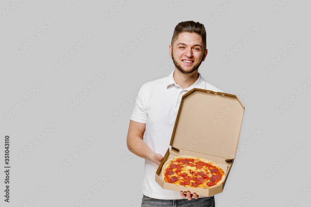 Online pizza safety delivery servise from restaurant. Pizza with cheese boards advertise. Isolated white background with empty space for advertise. Young caucasian courier man shows pizza and smile Online pizza safety delivery servise from restaurant. Pizza with cheese boards advertise. Isolated white background with empty space for advertise. Young caucasian courier man shows pizza and smile