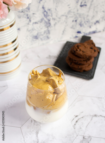 Angle view on dalgona coffee on marble surface with bouquet of flowers and chocolate chip cookies