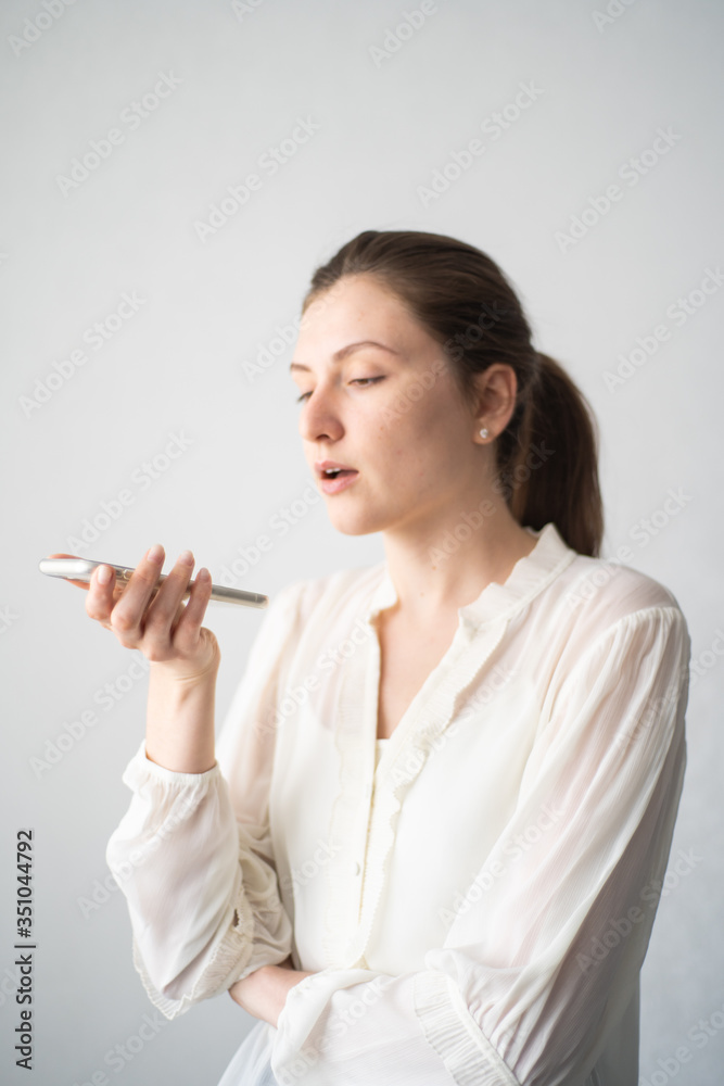 A millennial young woman activating a virtual assistant on a mobile phone. Ask a question to a voice assistant on a white background A millennial young woman activating a virtual assistant on a mobile phone. Ask a question to a voice assistant on a white background