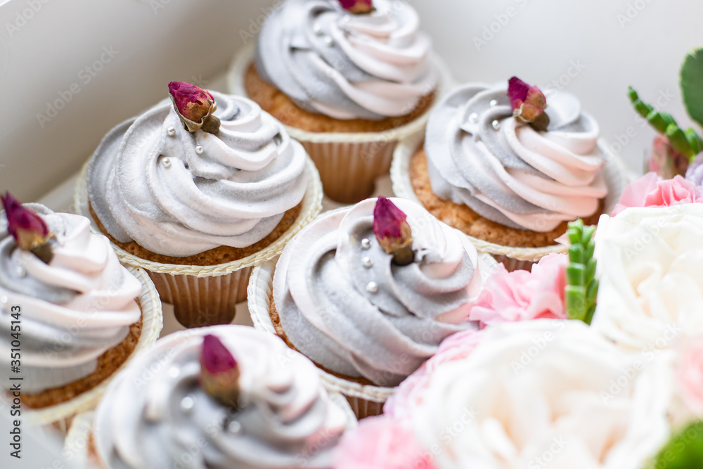 closeup of delicious sweet muffins with pink-gray butter cream in a box with flowers closeup of delicious sweet muffins with pink-gray butter cream in a box with flowers