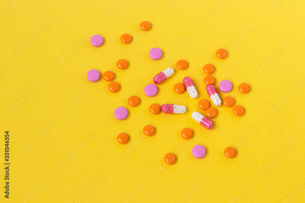Multi-colored pills are scattered on a bright yellow background, top view. Medication for the disease for patients. Dose drugs and vitamins for health. Copy space. Close up. Multi-colored pills are scattered on a bright yellow background, top view. Medication for the disease for patients. Dose drugs and vitamins for health. Copy space. Close up.