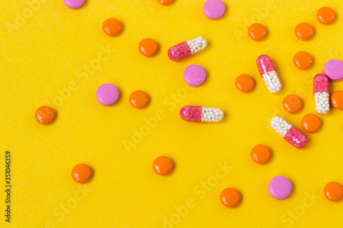 Multi-colored pills are scattered on a bright yellow background, top view. Medication for the disease for patients. Dose drugs and vitamins for health. Copy space. Close up.
