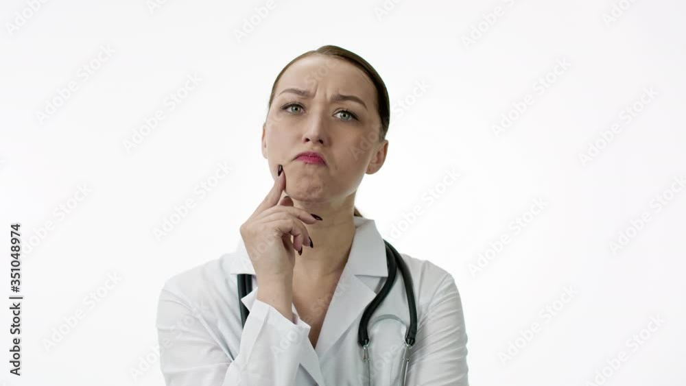 Attractive female therapist in medical coat with stethoscope over neck is very surprised, opens her mouth, holds her chin and scratches her head. Doctor reaction concept. Isolated on white background Attractive female therapist in medical coat with stethoscope over neck is very surprised, opens her mouth, holds her chin and scratches her head. Doctor reaction concept. Isolated on white background