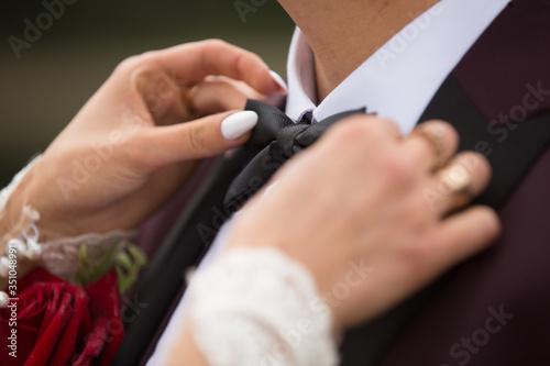 Hands of the bride on the groom s bow tie.