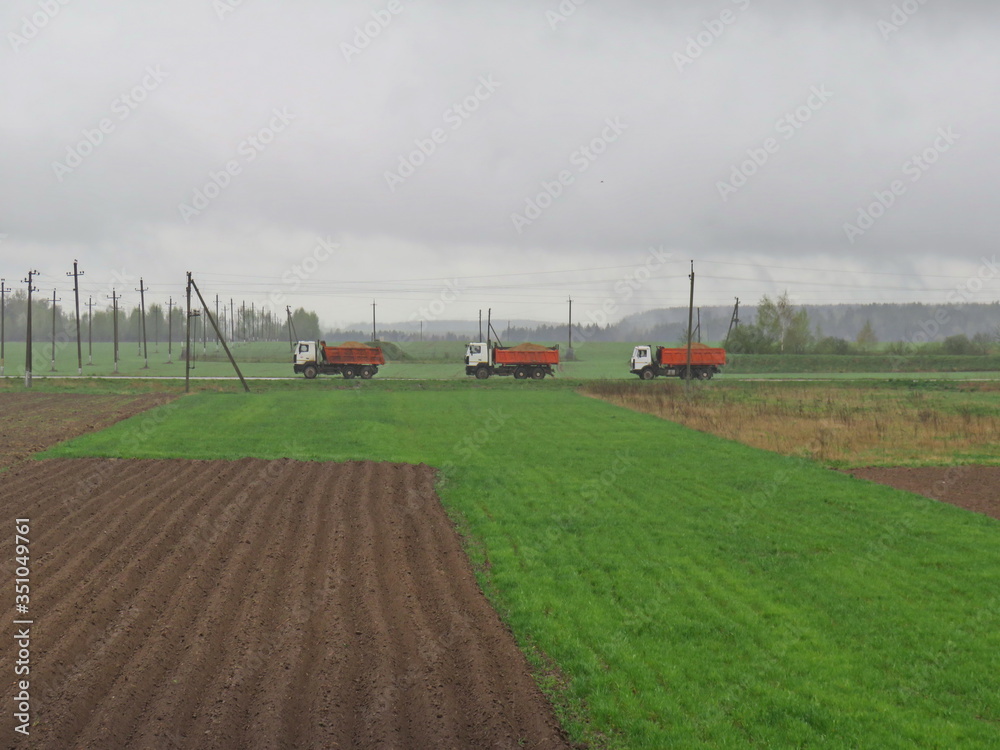 Three trucks carry sand for the construction of the road. Country road. Belarus landscape Three trucks carry sand for the construction of the road. Country road. Belarus landscape