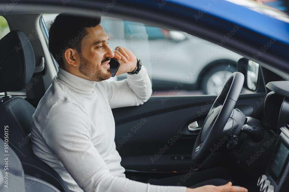 Handsome bearded businessman is sitting in a new car in car dealership Handsome bearded businessman is sitting in a new car in car dealership