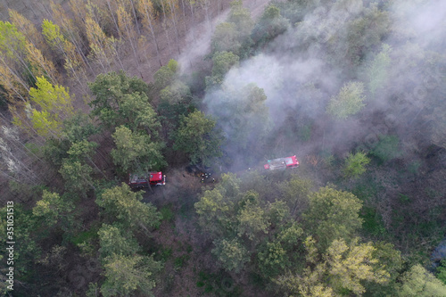 Forest and field fire. Burning of dry grass, natural disaster. Aerial view. After the fire, the ground is covered with a black and burning layer. Fire truck and firefighters extinguish the fire. 