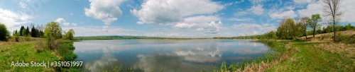 Panoramic landscape from the lake shore with colorful clouds in the spring sun.