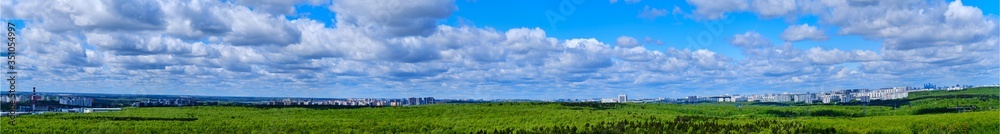 Panorama with a cloudy sky over a green forest. Summer park on a sunny day and the city behind the trees - Moscow, Russia, Butovo Panorama with a cloudy sky over a green forest. Summer park on a sunny day and the city behind the trees - Moscow, Russia, Butovo