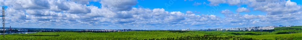 Panorama with a cloudy sky over a green forest. Summer park on a sunny day and the city behind the trees - Moscow, Russia, Butovo